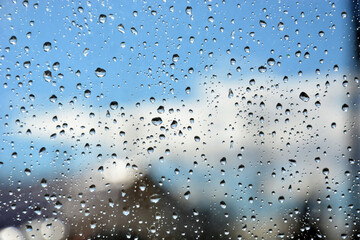 Naklejka na ściany i meble Raindrops on the transparent window pane. Background of raindrops on a wet, gray and opaque glass texture. Outside the window, rainy summer weather. Blurred background, urban landscape.