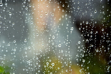 Raindrops on the transparent window pane. Background of raindrops on a wet, gray and opaque glass texture. Reflection in the window. Outside, the weather is rainy.