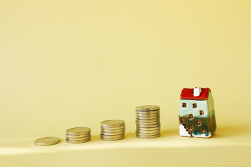 Piles of coins and a small house with a red roof on a yellow background. Concept - real estate investment, family budget or money to pay rent or purchase a home.