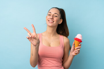 Young brunette woman with a cornet ice cream over isolated blue background smiling and showing victory sign