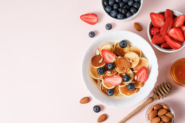 Pancake cereal with berries and honey on pink background
