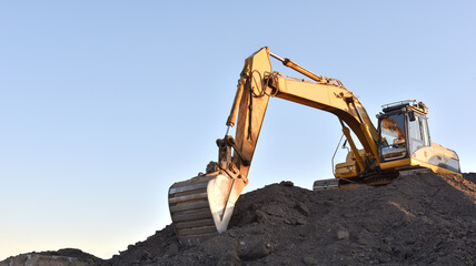 Yellow excavator during earthmoving at open pit on blue sky background. Construction machinery and...