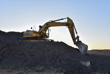 Yellow excavator during earthmoving at open pit on blue sky background. Construction machinery and earth-moving heavy equipment for excavation, loading, lifting and hauling of cargo on job sites