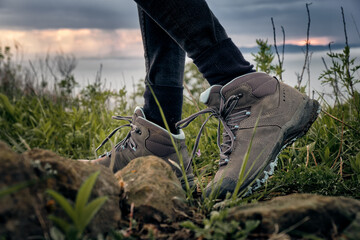 bottom side view on female hiking boots on green grass with sky background. Hiking and outdoor concept.