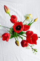 Bouquet of red tulips and daffodils on white tablecloth, top view