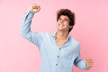 Young caucasian man with jean shirt over isolated pink background celebrating a victory