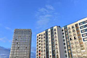 Fototapeta premium Facade of a new modern high-rise residential building. Skyscraper on blue sky background. Tall house renovation project, government programs. Minimalistic multi storied home. Urban architecture