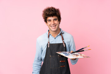 Young caucasian man over isolated pink background holding a palette