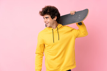 Young caucasian man over isolated pink background with skate and looking side