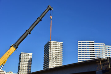 Fototapeta premium Crane hook on lifting gears and chains hanging of the mobile auto crane on a background residential building and blue sky. Concept of bridge construction