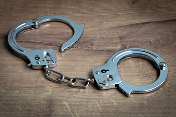 Steel handcuffs on a wooden background. Close-up.