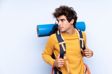 Young mountaineer man with a big backpack over isolated blue background