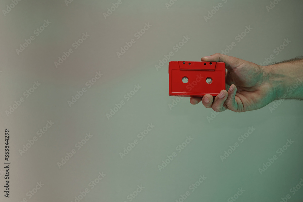 Poster Hand holding red audio cassette tape in the color light. Beautiful minimal in neon light. Minimalism retro style concept. Background pattern for design.