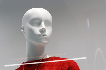 White plastic mannequin of a girl in a red sweater. Portrait of a mannequin behind glass on a shop...