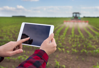 Farmer working on tablet in front of tractor in field
