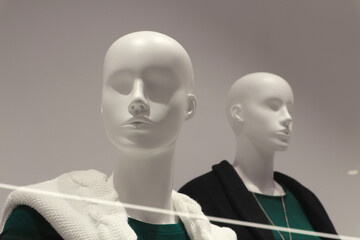 Two mannequins behind glass on a gray background.