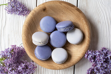 Macaroons in a wooden plate with lilac on a wooden background
