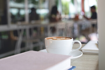 Cup of coffee and books on table in coffee shop coworking space with nobody