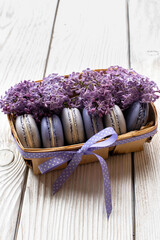 Purple macaroons with lilac in a basket on a wooden background