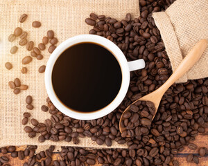 Closeup coffee cup and coffee beans on wooden background with the coffee sack and morning sunlight, black coffee in the morning concept
