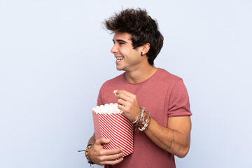 Young caucasian man over isolated background with 3d glasses and holding a big bucket of popcorns