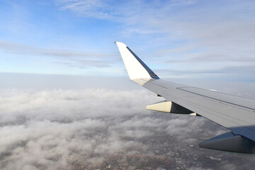Airplane wing view from window, flying above white clouds on the sky