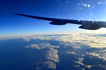 Silhouette of Airplan wing flying above cloudscrape in horizon blue sky with sunlight,  view from airplane window.