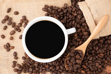 Closeup coffee cup and coffee beans on wooden background with the coffee sack and morning sunlight, black coffee in the morning concept
