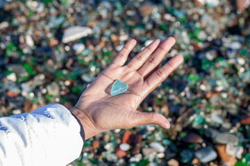 A brown indian hand holding a light glass piece shaped as heart by sea