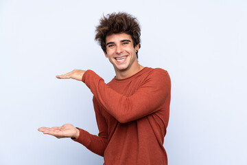 Young caucasian man over isolated blue background holding copyspace to insert an ad