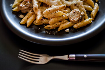 penne pasta and boscaiola topping sauce in a dish with fork closeup
