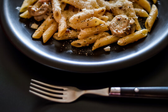 penne pasta and boscaiola topping sauce in a dish with fork closeup