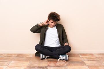 Young caucasian man sitting on the floor with neckache