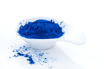 Blue spirulina powder isolated on white background. Phycocyanin extract. Natural superfood. Vegan, healthy dietary supplement, close up of blue spirulina algae powder in white spoon on white table