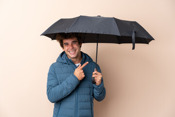 Man holding an umbrella over isolated background and pointing it