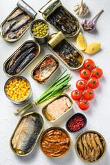Assortment of canned preserves  food in tin  open cans. with fresh organic ingridients Saury, mackerel, sprats, sardines, pilchard, mango ,  beans,   over white textured background  top view vertical