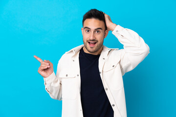 Young handsome man over isolated blue background surprised and pointing finger to the side