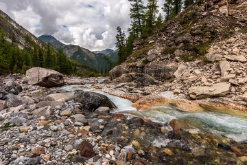 Large boulders next to a mountain stream. A lot of stones around. Mountains with clouds in the distance. Horizontal.