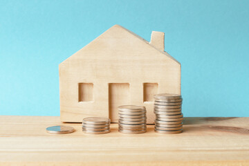 Piles of coins and a wooden  house on a blue background. Concept - real estate investment, family...