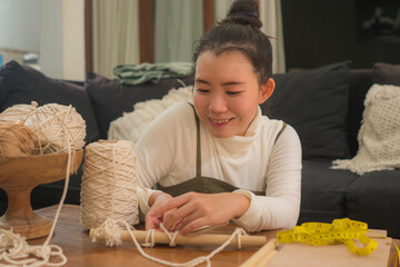 Asian girl enjoying macrame handcraft hobby - young happy and pretty Korean woman at home doing...