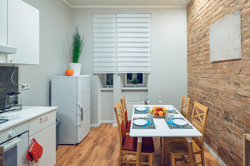 Modern contemporary interior of kitchen in loft apartment. Brick wall. Table and chairs. Fridge. White kicthen set.