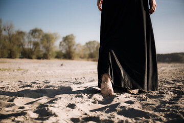 A woman walks into the distance on the sand with her bare feet. Black and white photo of a part of...