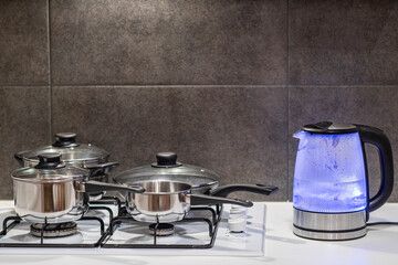 Modern interior of kitchen. The boiled kettle. Stove with pots and pans.