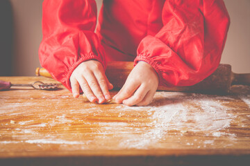 The concept of homemade pastry. Cute little child girl chef cooking cakes dough on wooden desk with flour.