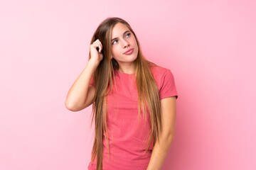 Teenager blonde girl over isolated pink background having doubts and with confuse face expression