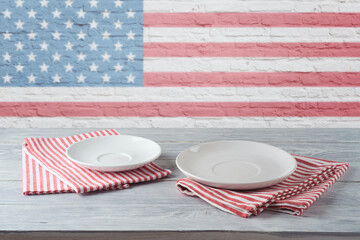 Empty plate with stripes tablecloth on wooden table over brick wall with american flag. 4th of july USA independence day mock up for design.