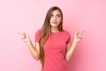 Teenager blonde girl over isolated pink background pointing to the laterals having doubts