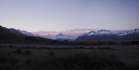 Beautiful panoramic view of a snowy mountain on an open field during sunset with purple sky color cast