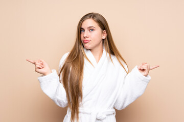 Teenager girl in a bathrobe over isolated background pointing to the laterals having doubts