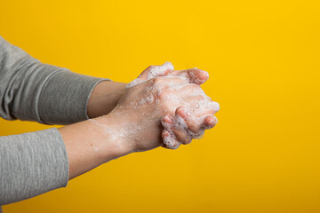 Fototapeta premium Instruction to carefully wash your hands and nails on a yellow background. Women's hands in a soap solution on a bright background